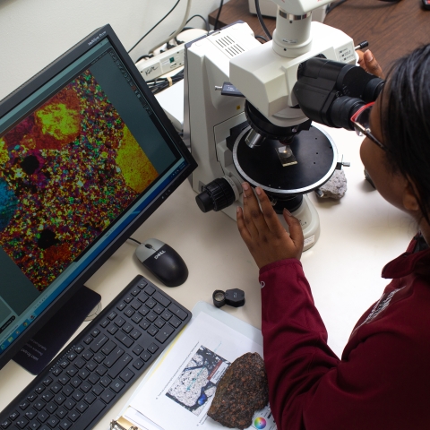 Woman looks at cells through a microscope.