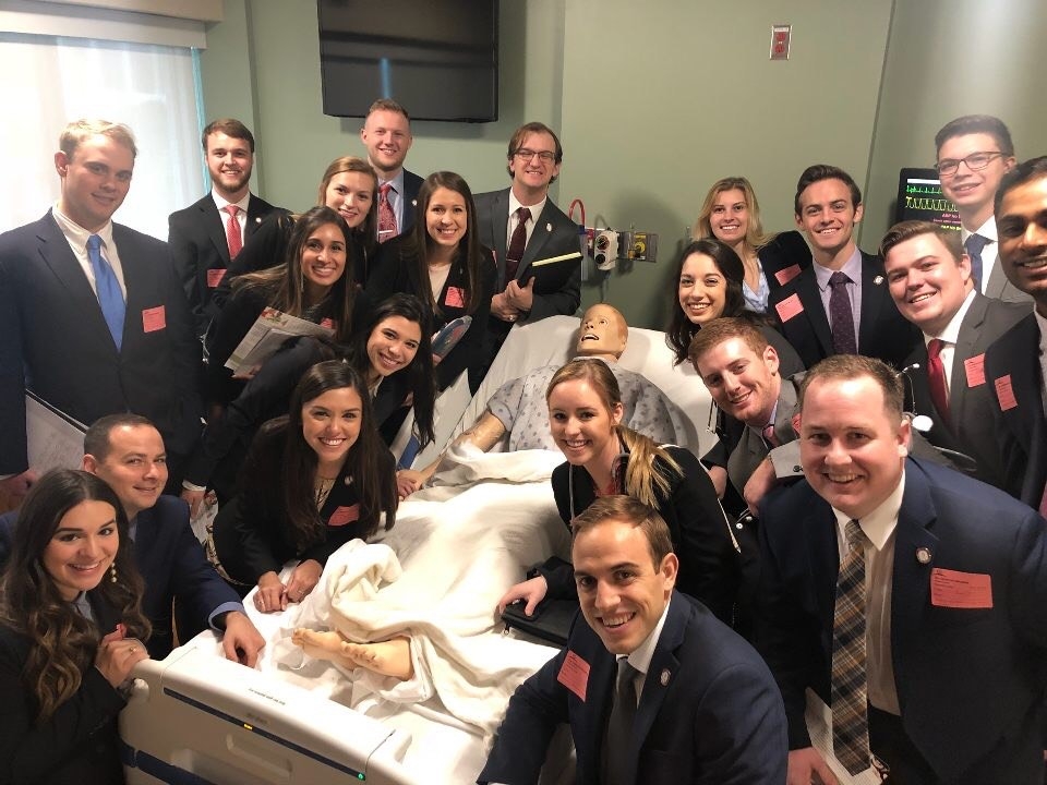 Students pose with mannequin of a patient on a gurney.