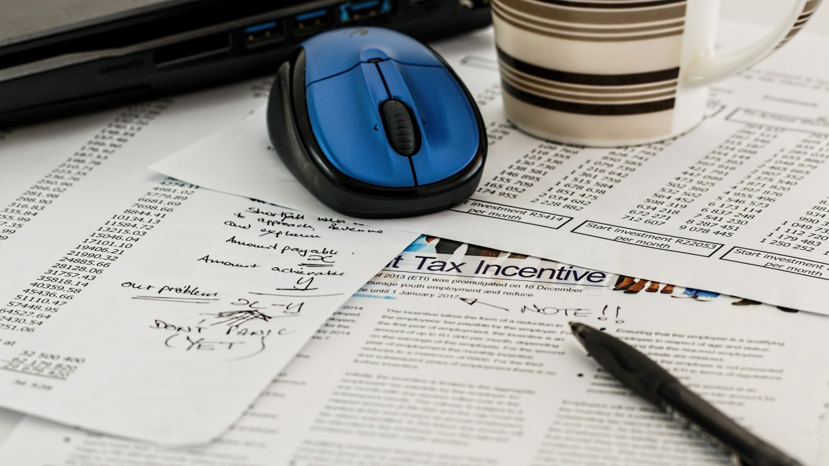 various financial forms with a pen and computer mouse on a table