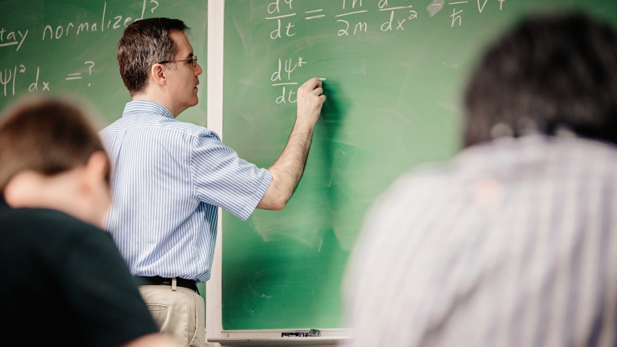 Professor at the chalkboard writing out equations
