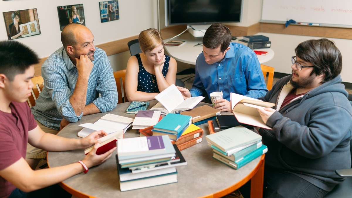 Professor and students sitting around a table discussing a book