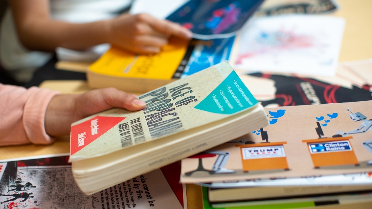 Student hand holding a textbook with other books piled underneath