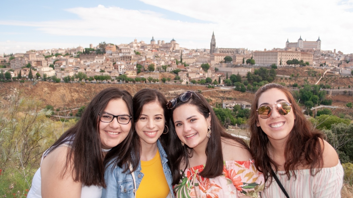 four young women smile with an old spanish town visible in the distance 