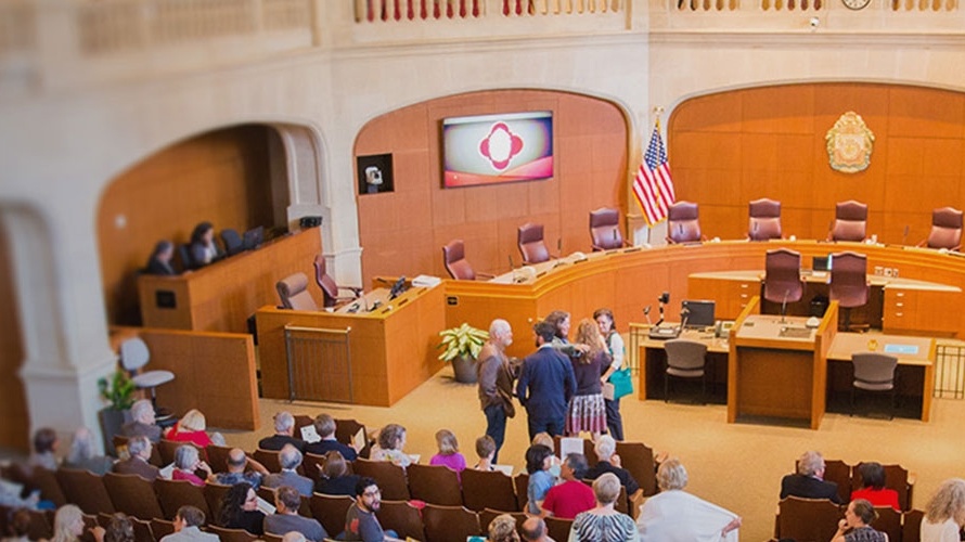 Government officials and community members gather together in council room for a hearing.