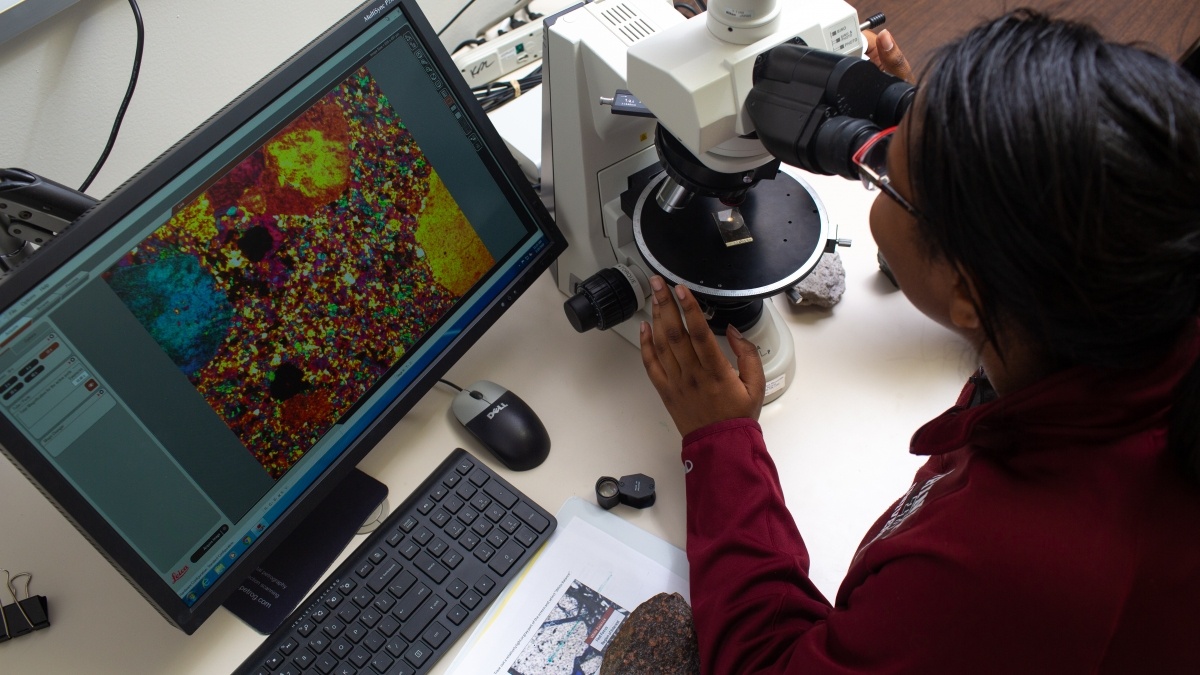 Woman looks at cells through a microscope.