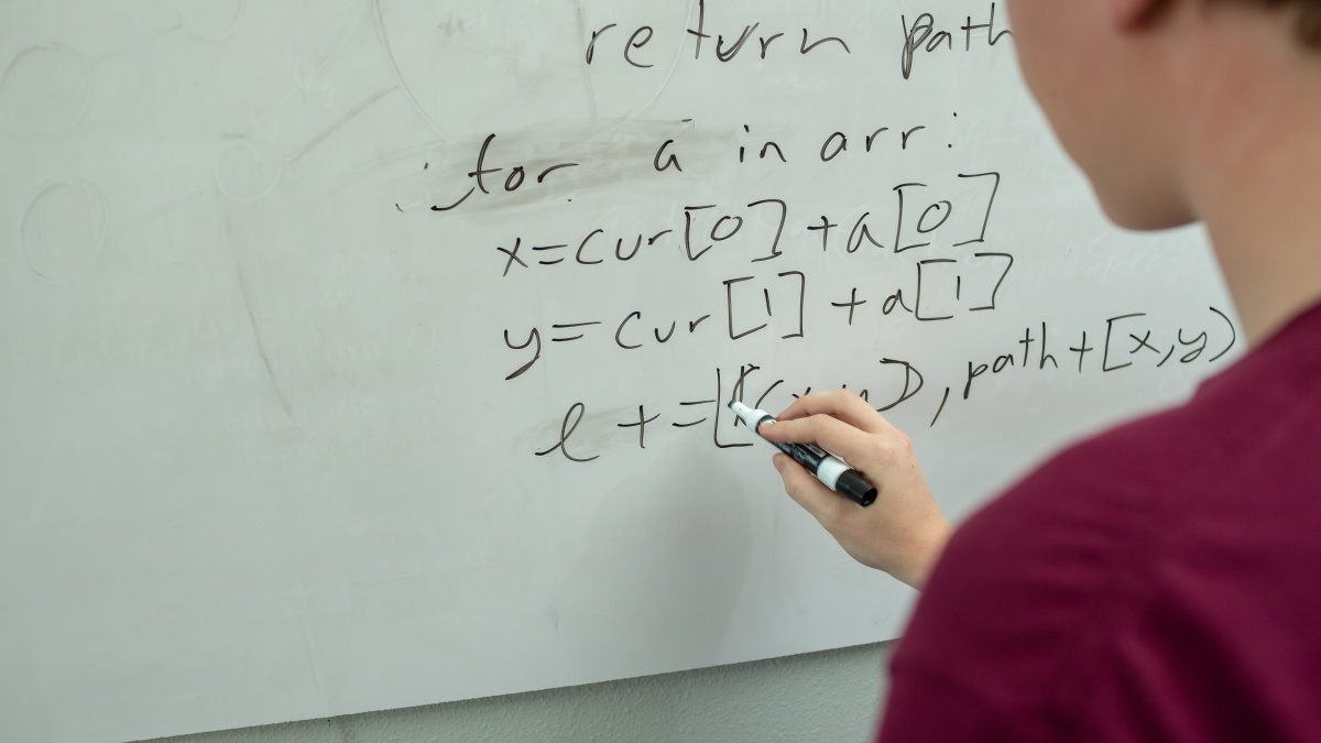 person writing equations on a white board