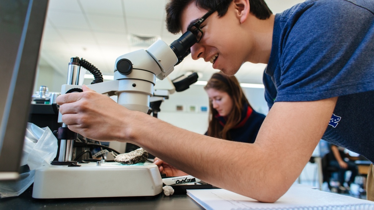 Student looking into a microscope with another student in the background
