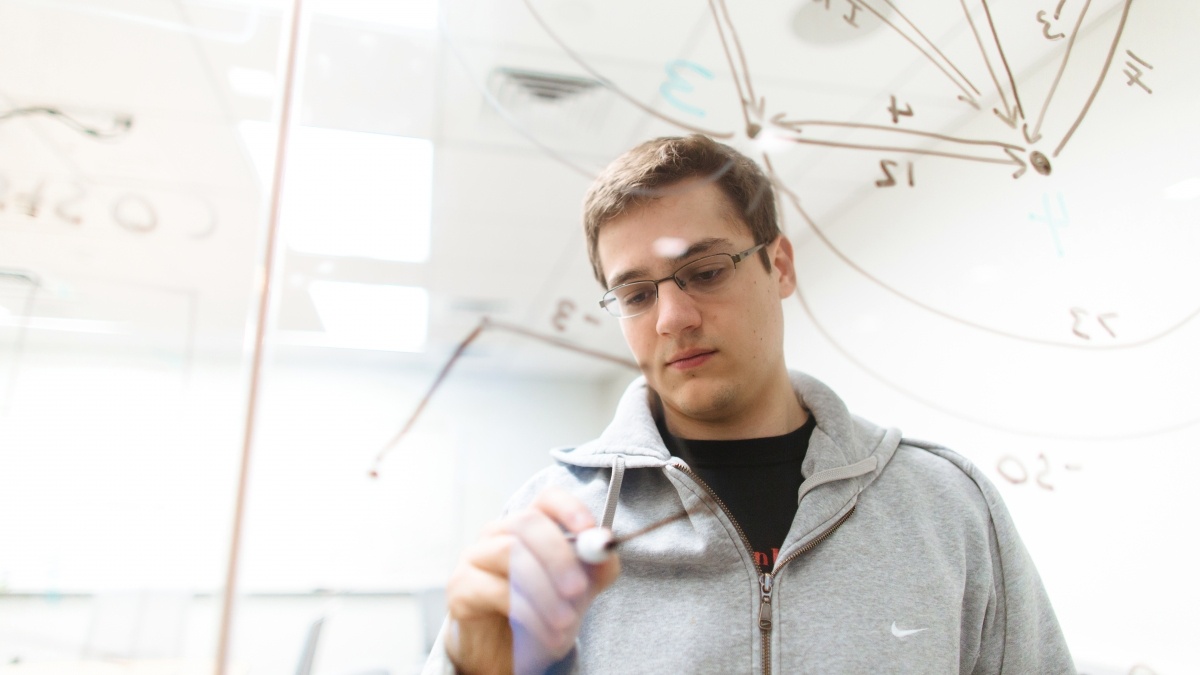 Student writing analytics and equations on a clear window