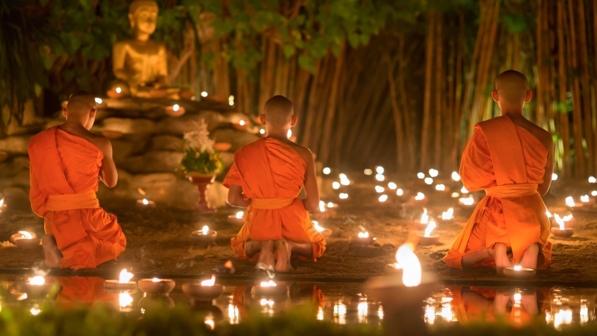Buddhists kneeling in the dark surrounded by candles with a statue of the Buddha in the background