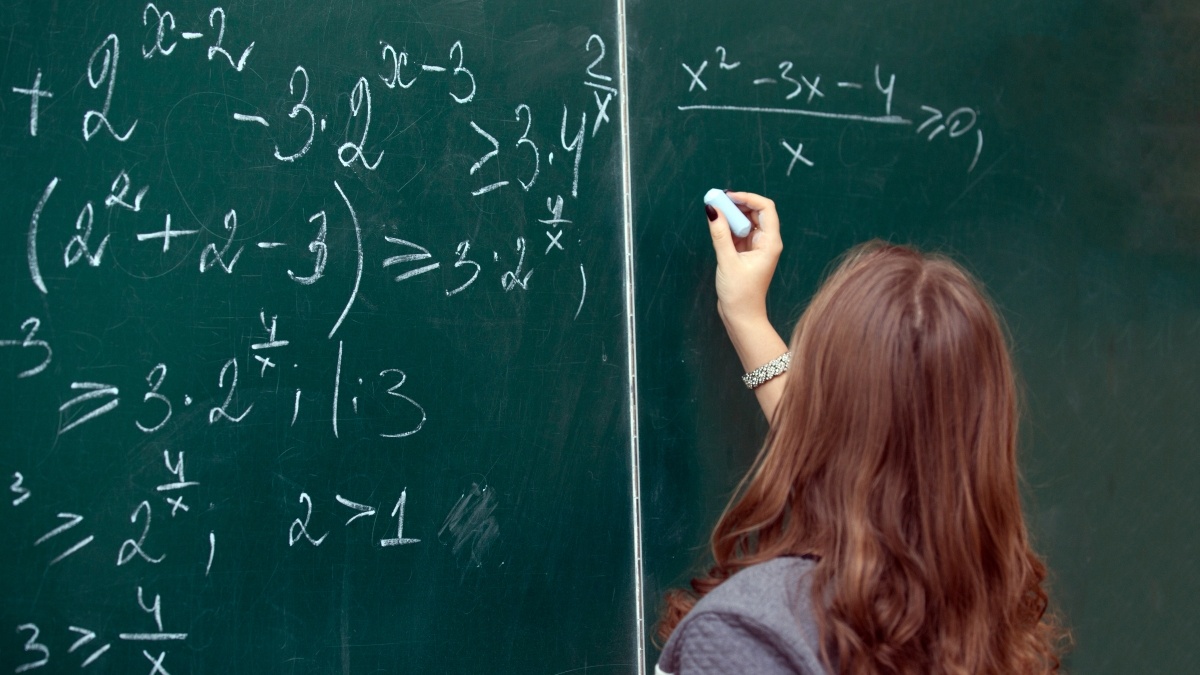 Female student solves a math problem on a chalkboard.